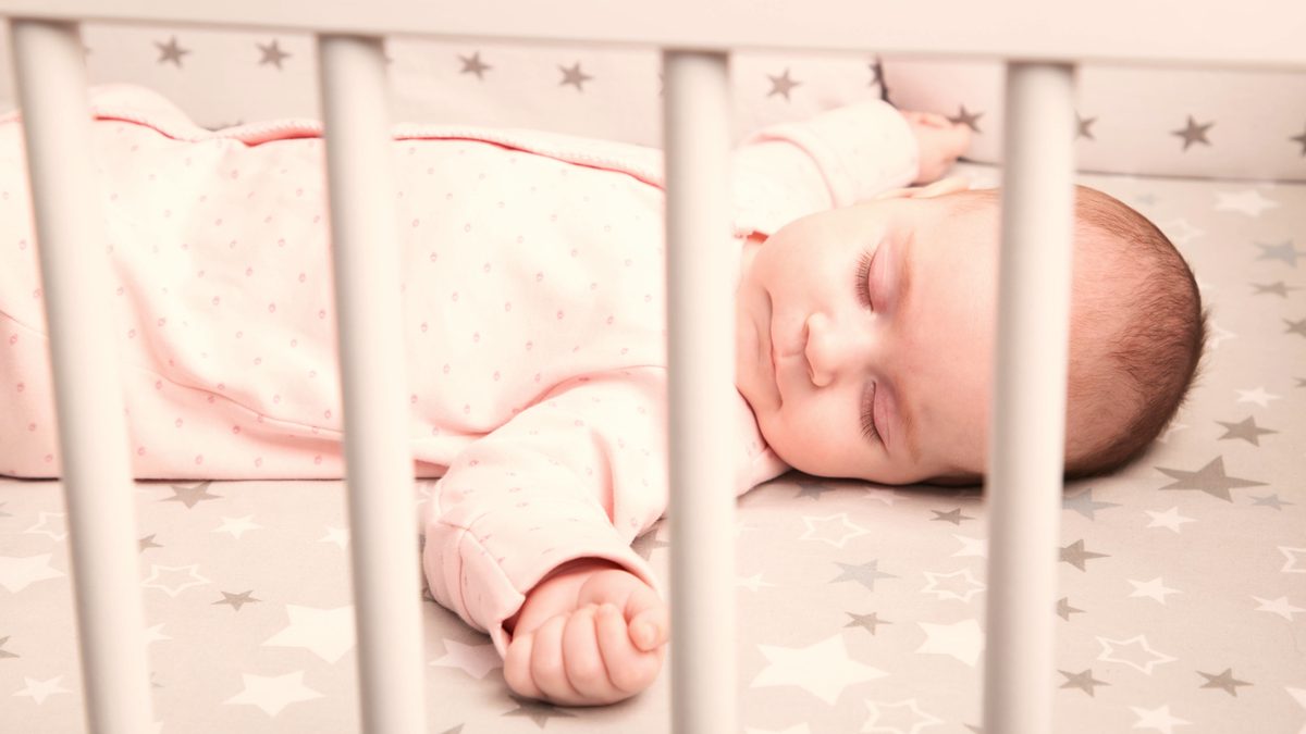 Bébé endormi sur le dos dans un lit à barreaux adapté