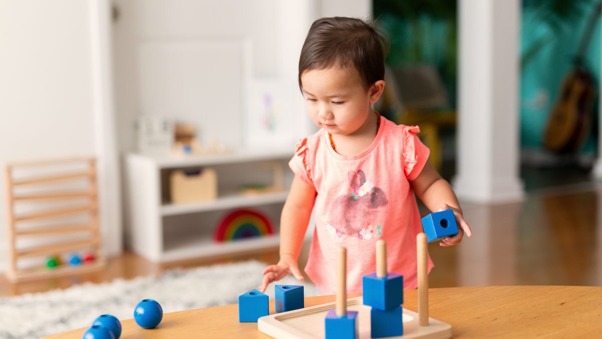 Jeune enfant manipulant du matériel Montessori en bois posé sur une table basse