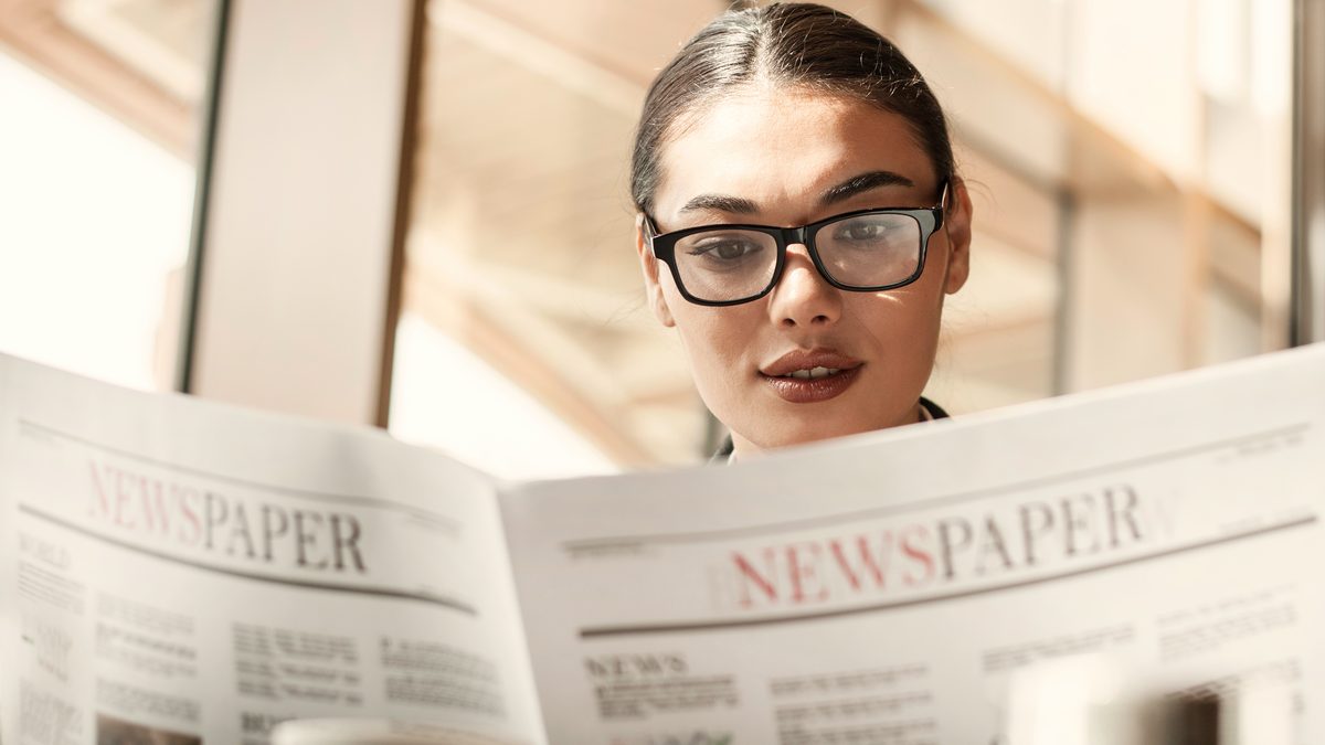 Jeune femme à lunettes lisant attentivement un journal
