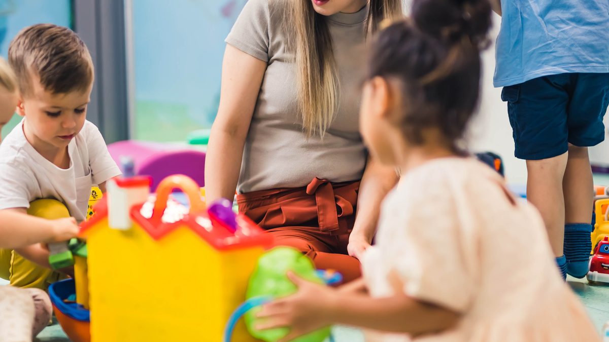 Professionnelle de crèche accompagnant plusieurs jeunes enfants pendant un temps de jeu en collectivité