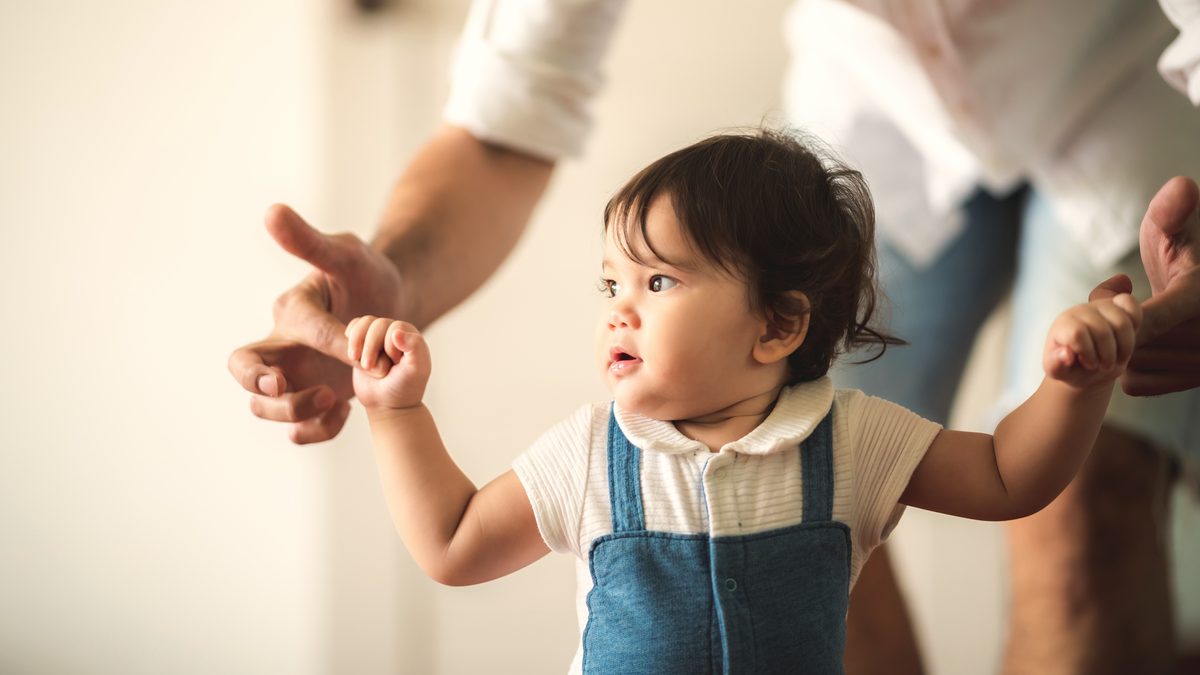 Bébé faisant ses premiers pas en tenant les mains de ses parents