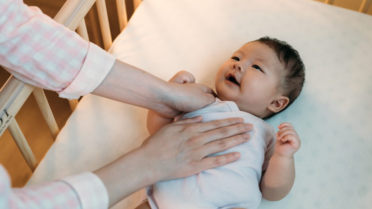 Parent posant doucement la main sur la poitrine de son bébé installé dans son lit