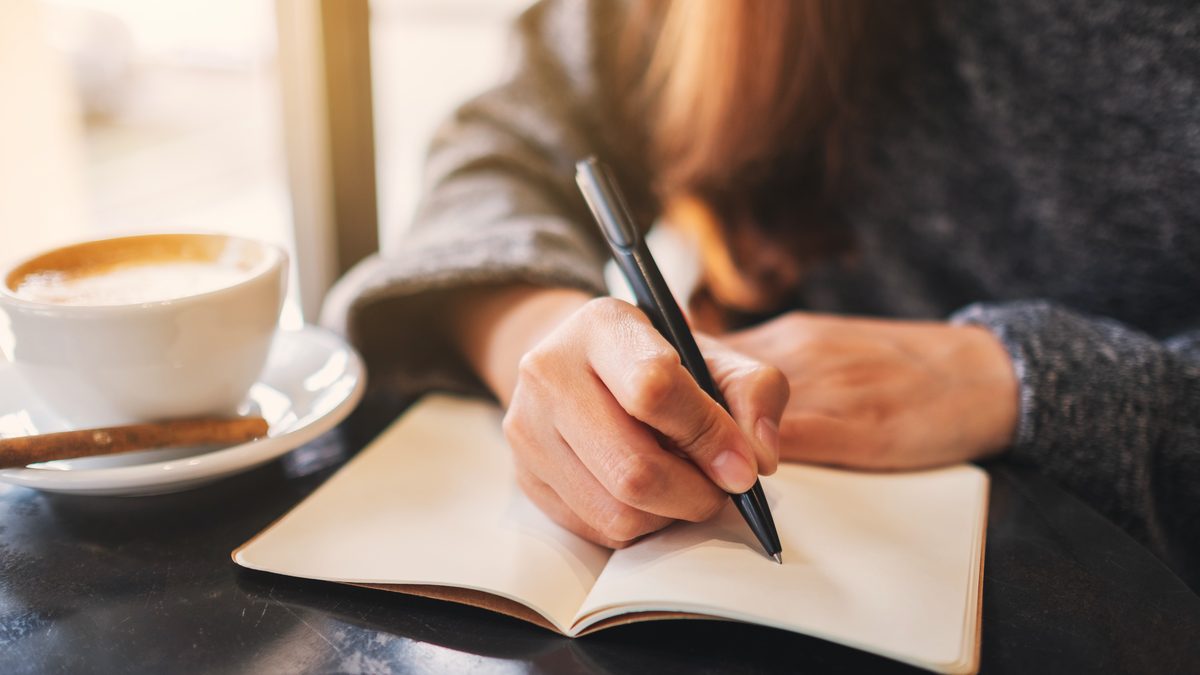 Candidate rédigeant une analyse de situation professionnelle dans un carnet, café à côté