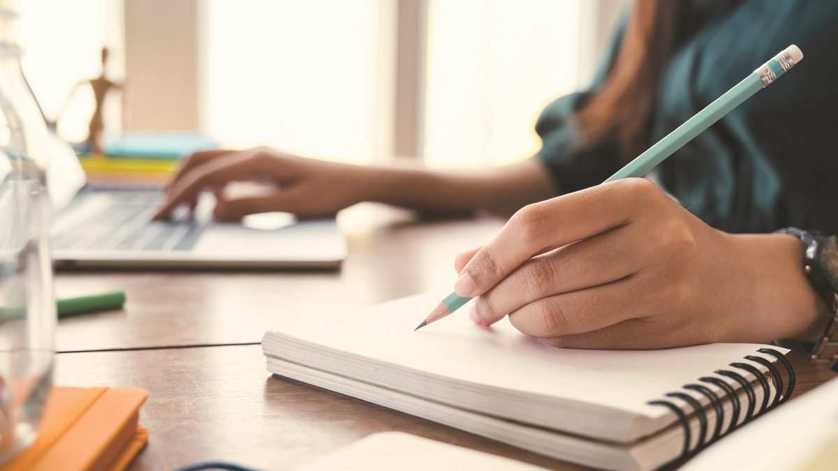 Mains qui écrivent des notes dans un cahier ouvert sur un bureau