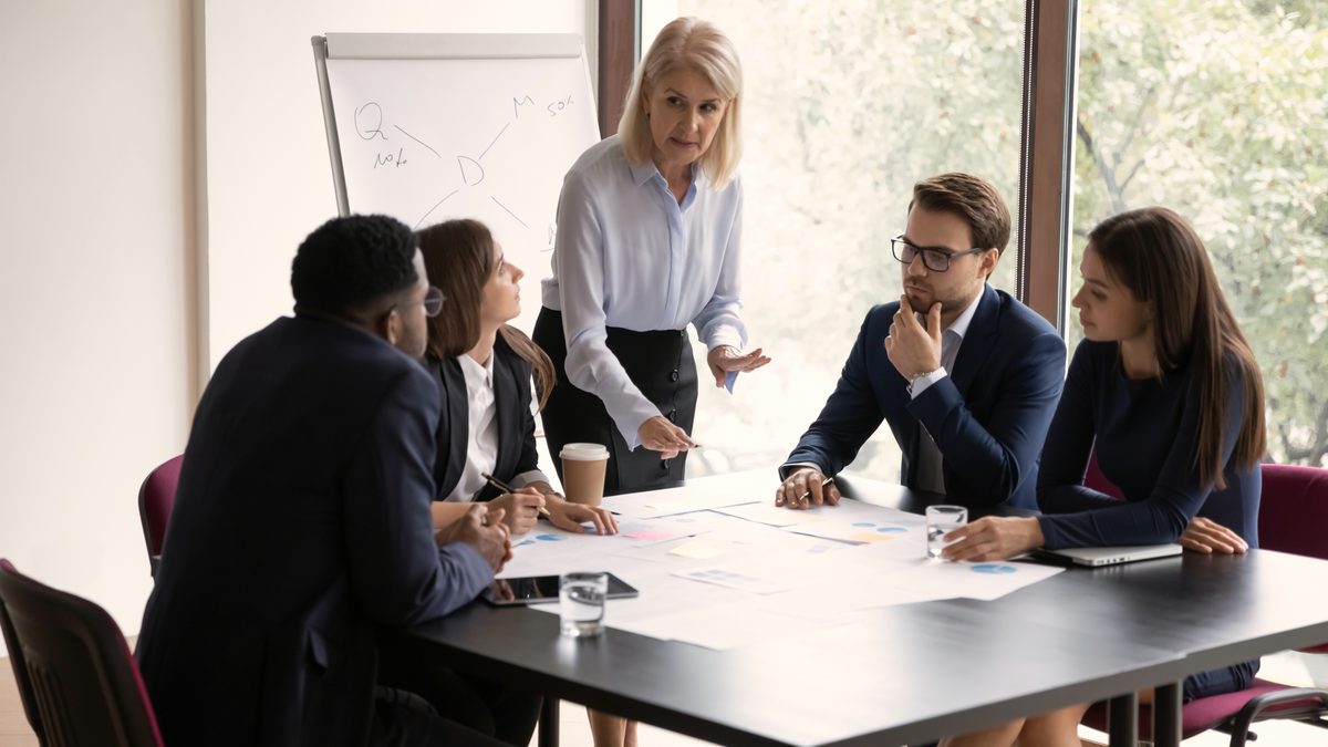 Une responsable anime une réunion d'équipe autour d'une grande table couverte de documents de travail