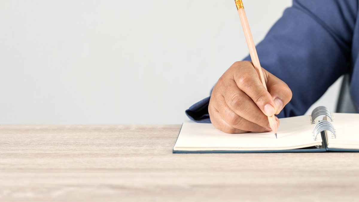 Main d'une adulte en formation prenant des notes dans un carnet posé sur une table claire