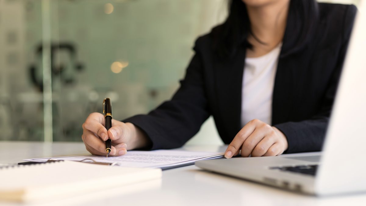 Une femme signe un document professionnel avec un stylo, sur un bureau