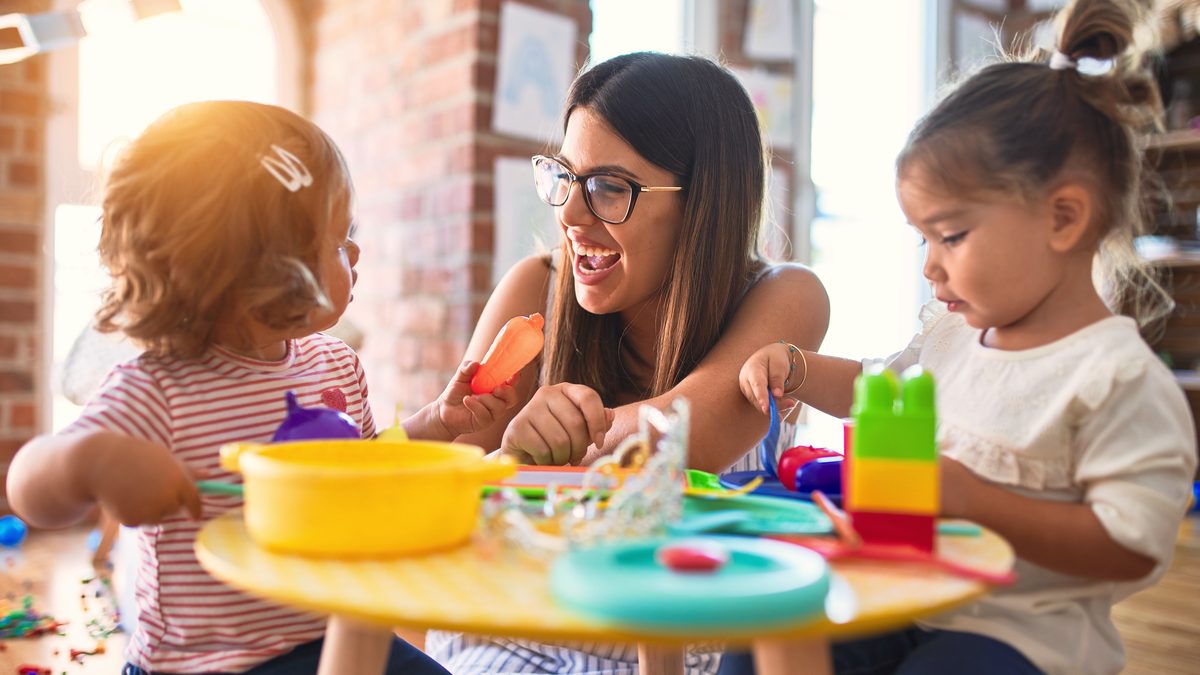 Professionnelle de la petite enfance animant un jeu d'imitation autour d'une table avec de jeunes enfants