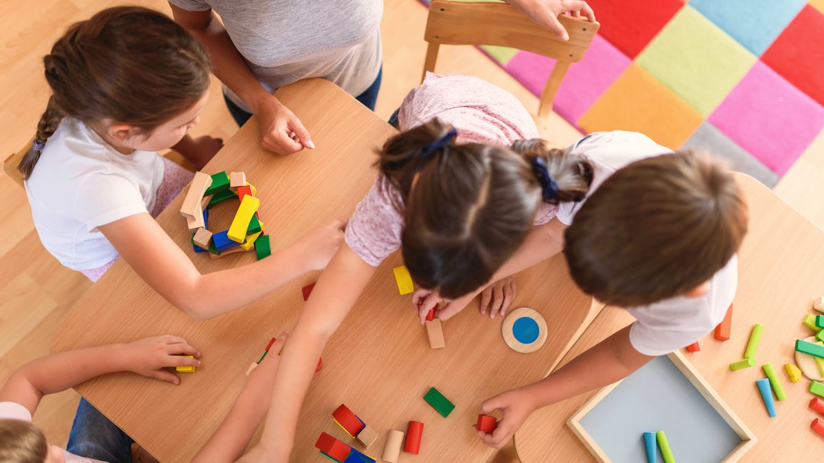 Table d'activité en structure petite enfance avec jeux de construction en bois et enfants accompagnés par une professionnelle