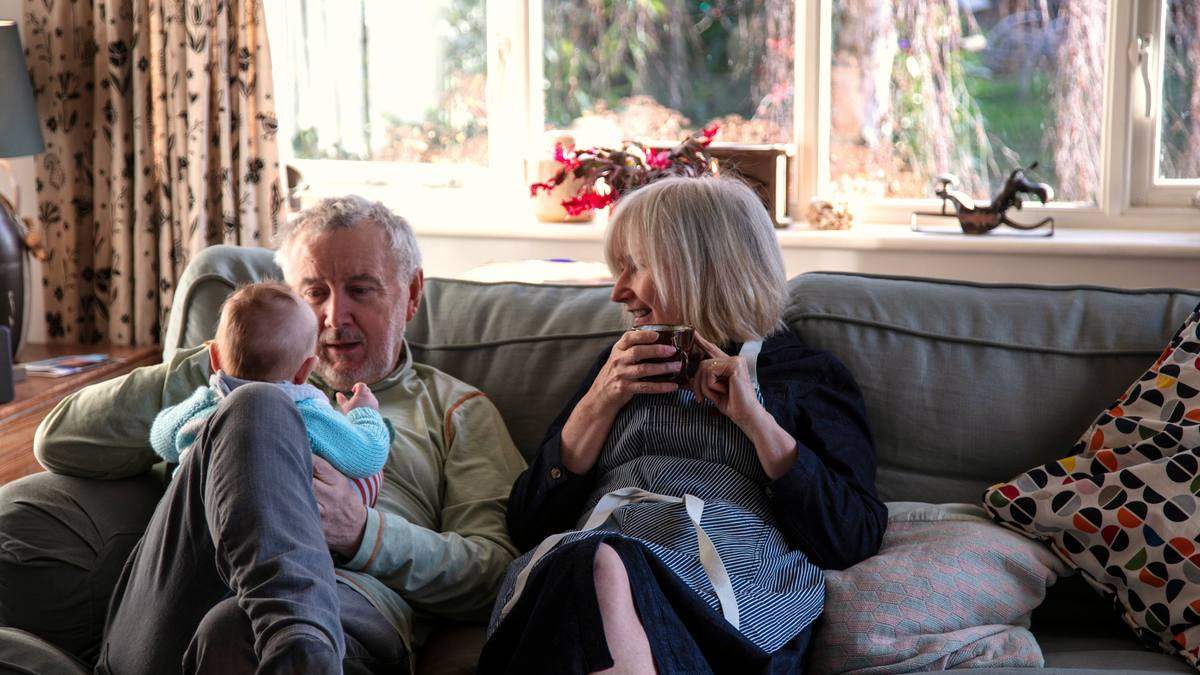 Grands-parents installés dans leur salon avec leur petit-enfant dans les bras
