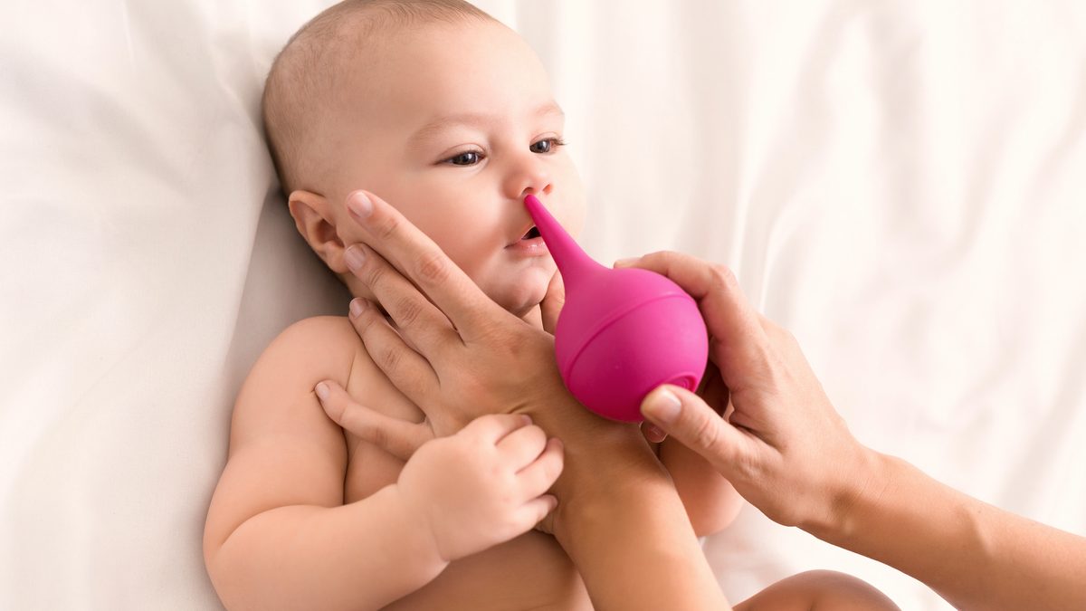 Un nourrisson allongé sur le dos, un adulte lui lave le nez avec une poire de lavage