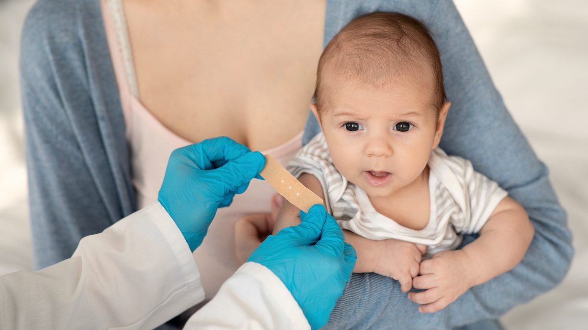 Une infirmière en gants bleus pose un pansement sur le bras d'un nourrisson tenu par sa mère