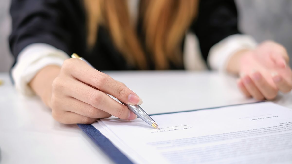 Mains d'une jeune femme tenant un stylo au-dessus d'un contrat de travail posé sur un bureau