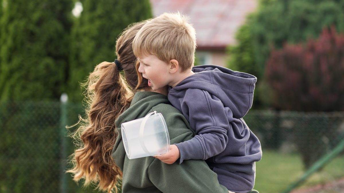 Une mère porte dans ses bras son jeune enfant en pleurs et le console à l'extérieur