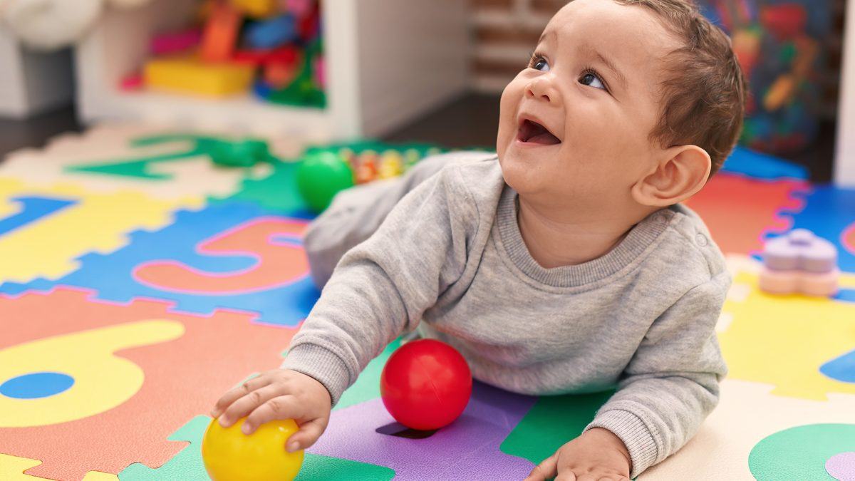 Bébé souriant jouant au sol sur un tapis d'éveil dans une section de crèche