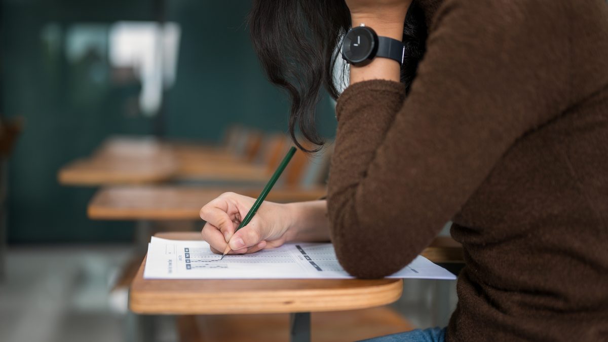 Adulte assise à une table d'examen, en train de rédiger sur une copie