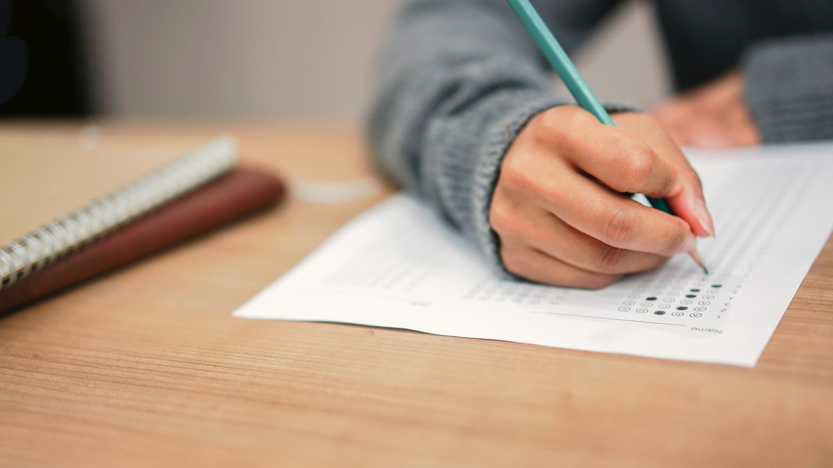 Main écrivant au crayon sur une feuille de réponses posée sur une table en bois