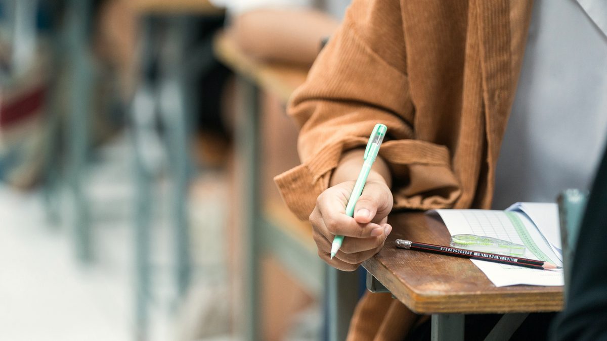 Main d'une candidate écrivant sur une copie à son pupitre pendant une épreuve de concours