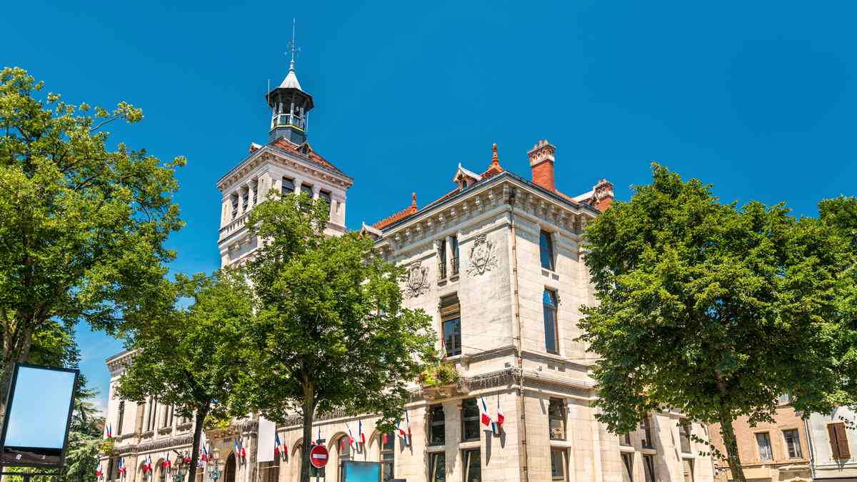 Mairie française avec tour de l'horloge et drapeaux tricolores, entourée d'arbres