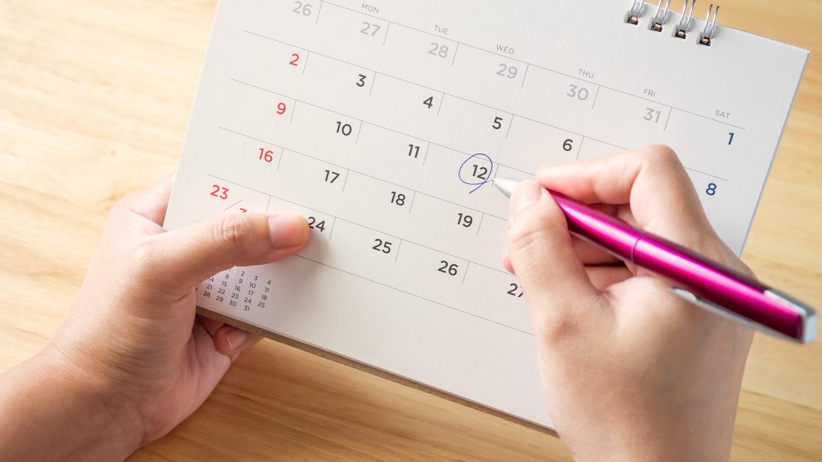 Deux mains cerclent une date au stylo sur un calendrier de bureau en papier