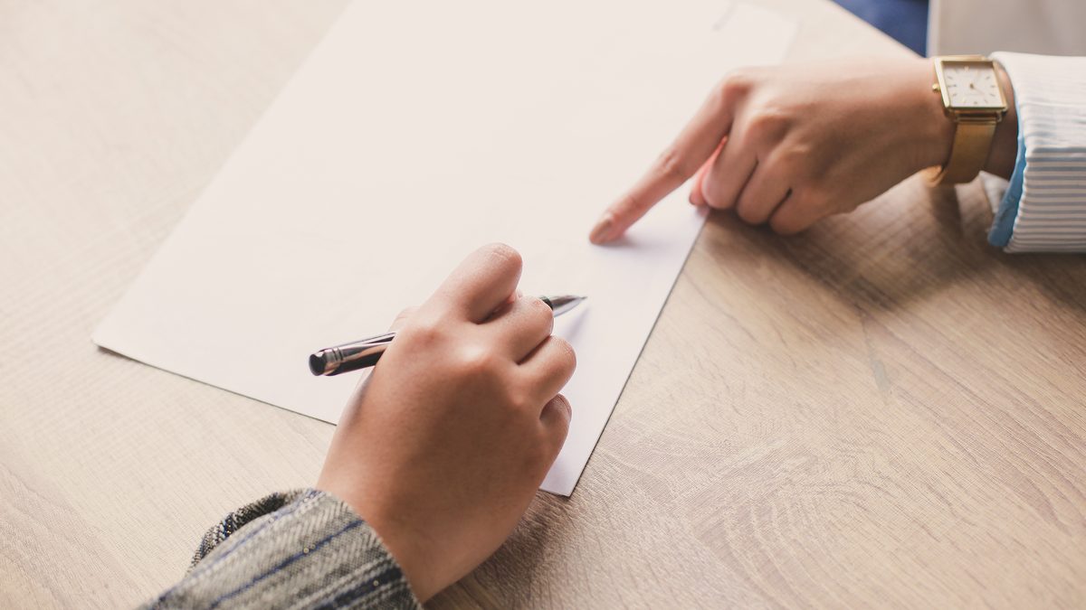 Deux personnes assises &agrave; un bureau devant un document, l'une tenant un stylo avant de signer