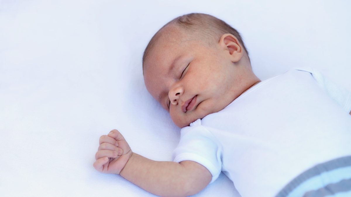 Un nouveau-né dort sur le dos, sur un drap blanc nu