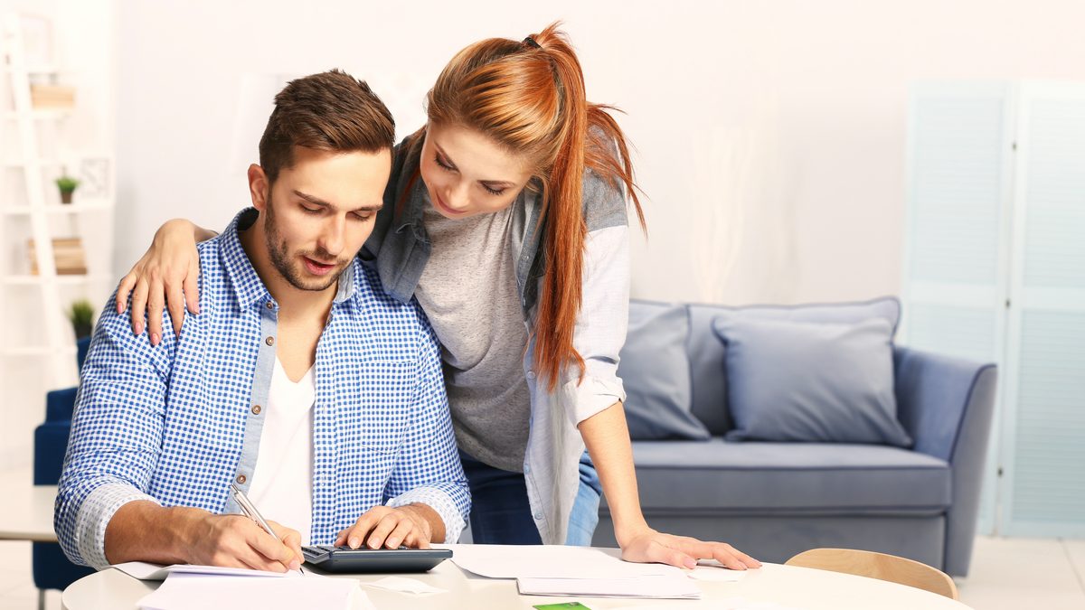 Un couple installé à table fait ses comptes avec une calculatrice et des documents, pour estimer le budget de la crèche