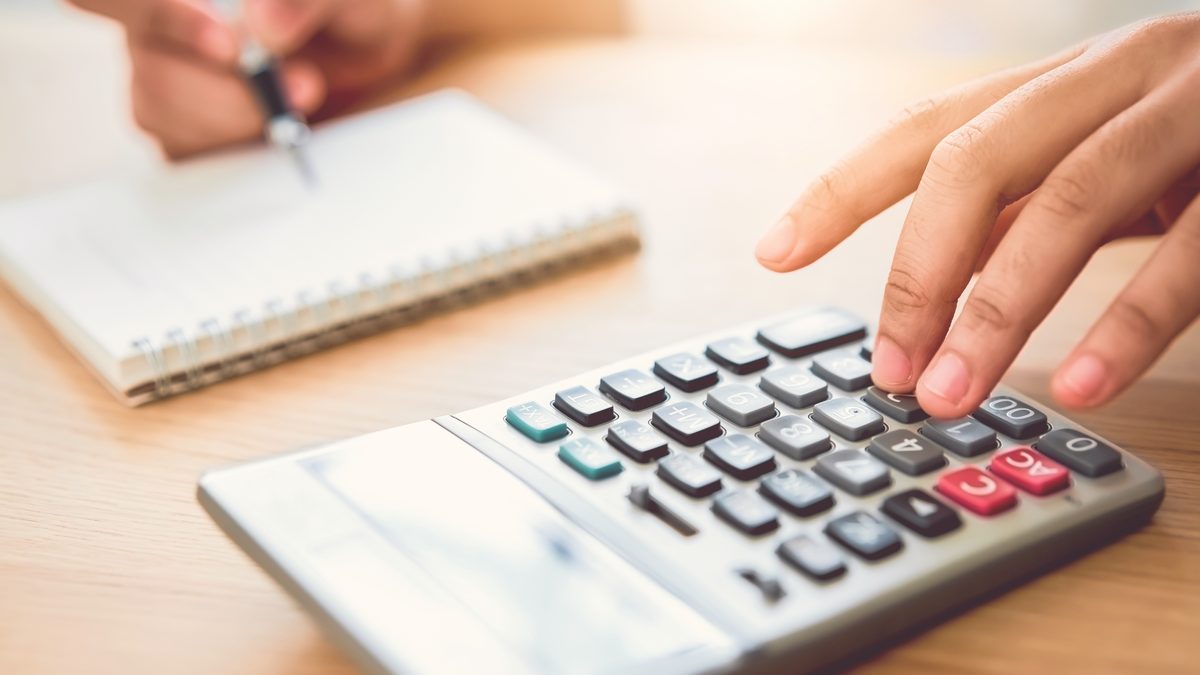 Main d'une femme sur une calculatrice à côté d'un carnet, pour établir le budget d'une formation