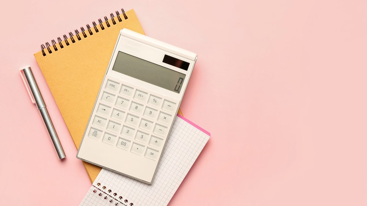 Une calculatrice blanche posée sur un carnet et une feuille quadrillée, avec un stylo, sur fond rose