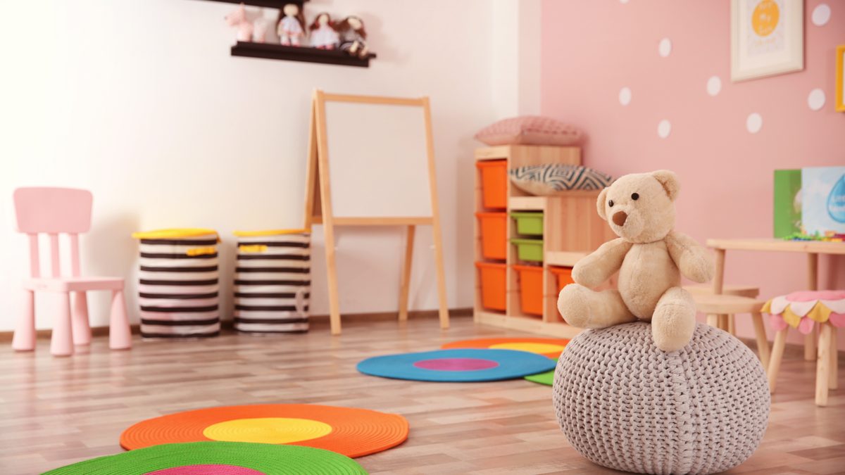 Une salle d'accueil claire et colorée, avec petites chaises, tapis ronds, chevalet et ours en peluche, prête à recevoir de jeunes enfants