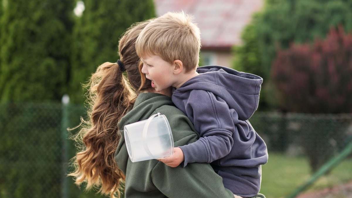 Mère portant son jeune enfant contrarié dans ses bras, dehors en fin de journée