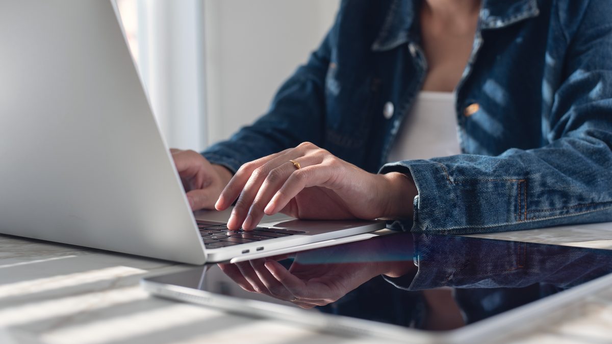 Mains d'une femme sur le clavier d'un ordinateur portable posé sur une table, près d'une fenêtre