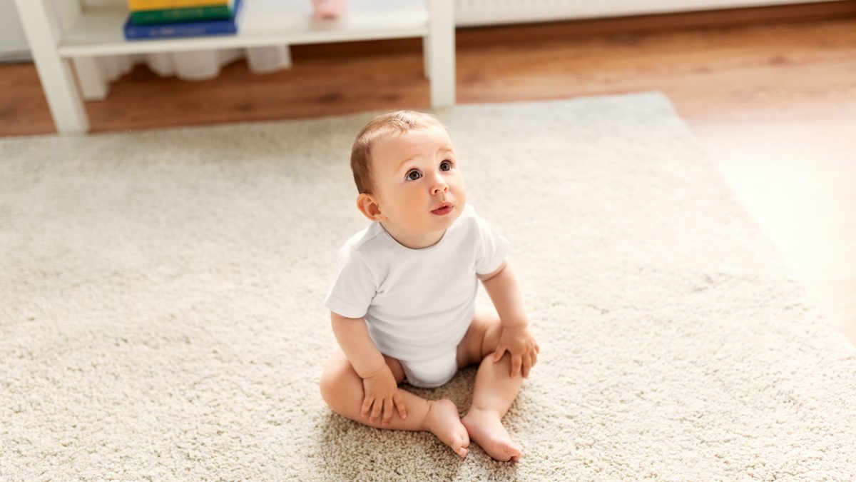 Bébé assis sur un tapis dans un salon, en pleine découverte de son environnement