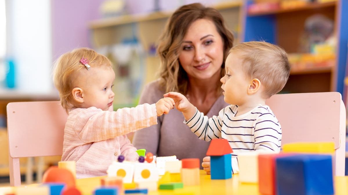 Auxiliaire de puériculture accompagnant deux jeunes enfants pendant un jeu en crèche