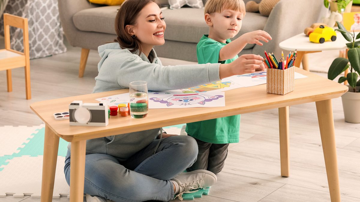 Une assistante maternelle dessine avec un petit garçon autour d'une table basse