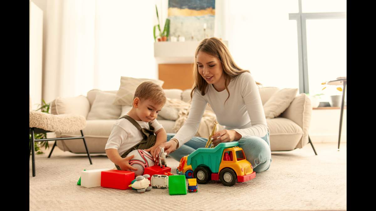 Une assistante maternelle assise dans son salon avec un jeune enfant, intérieur chaleureux et lumineux