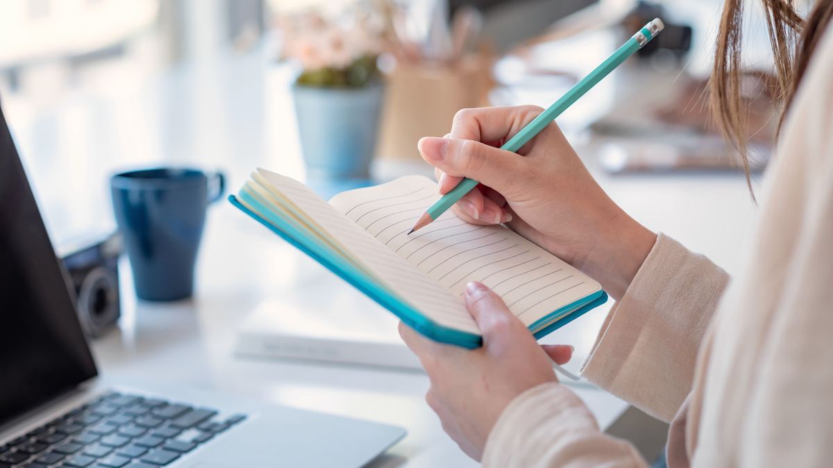 Femme prenant des notes dans un carnet à son bureau, préparation d'un projet de reconversion petite enfance
