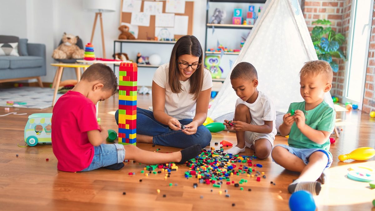 Une professionnelle de la petite enfance joue avec trois jeunes enfants sur le sol d'une salle de jeux lumineuse
