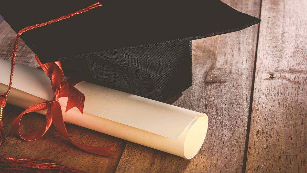 Toque de diplômé et parchemin noué d'un ruban posés sur une table en bois