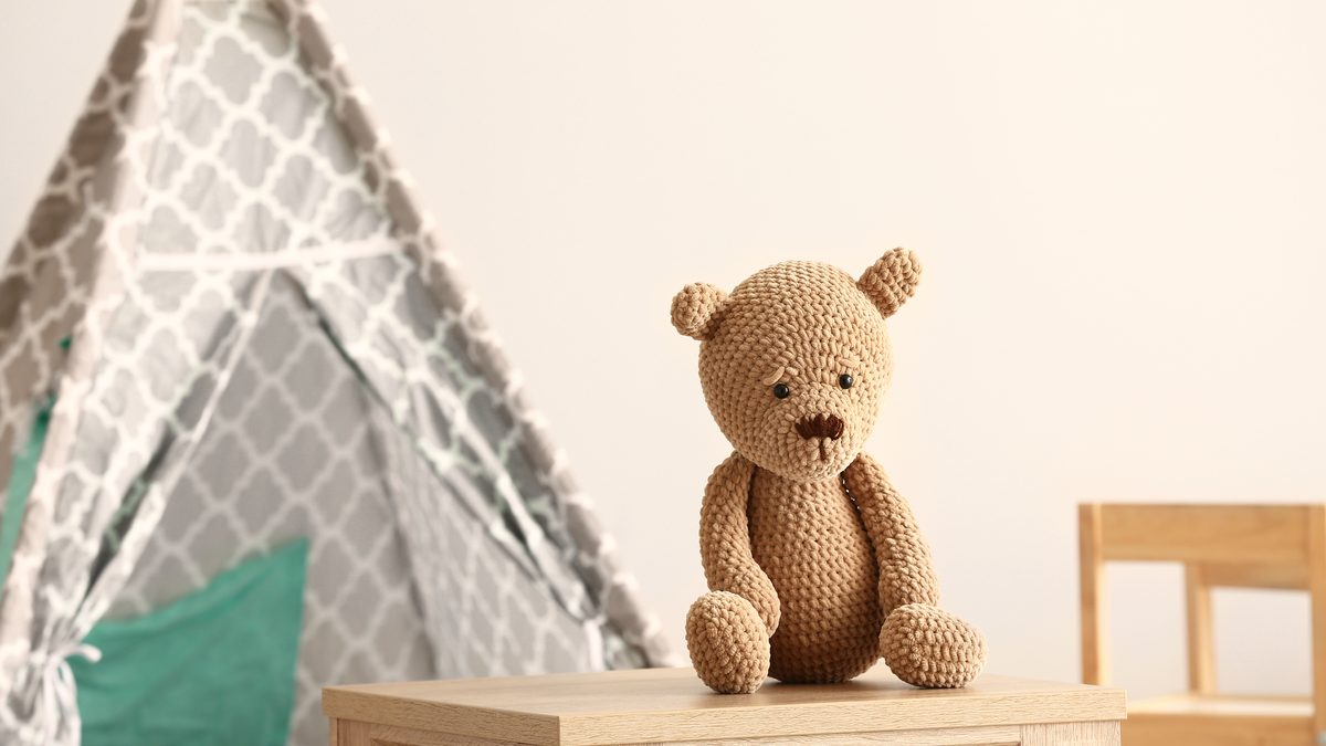 Petit ours en peluche posé sur un meuble en bois dans une chambre d'enfant, près d'une tente de jeu