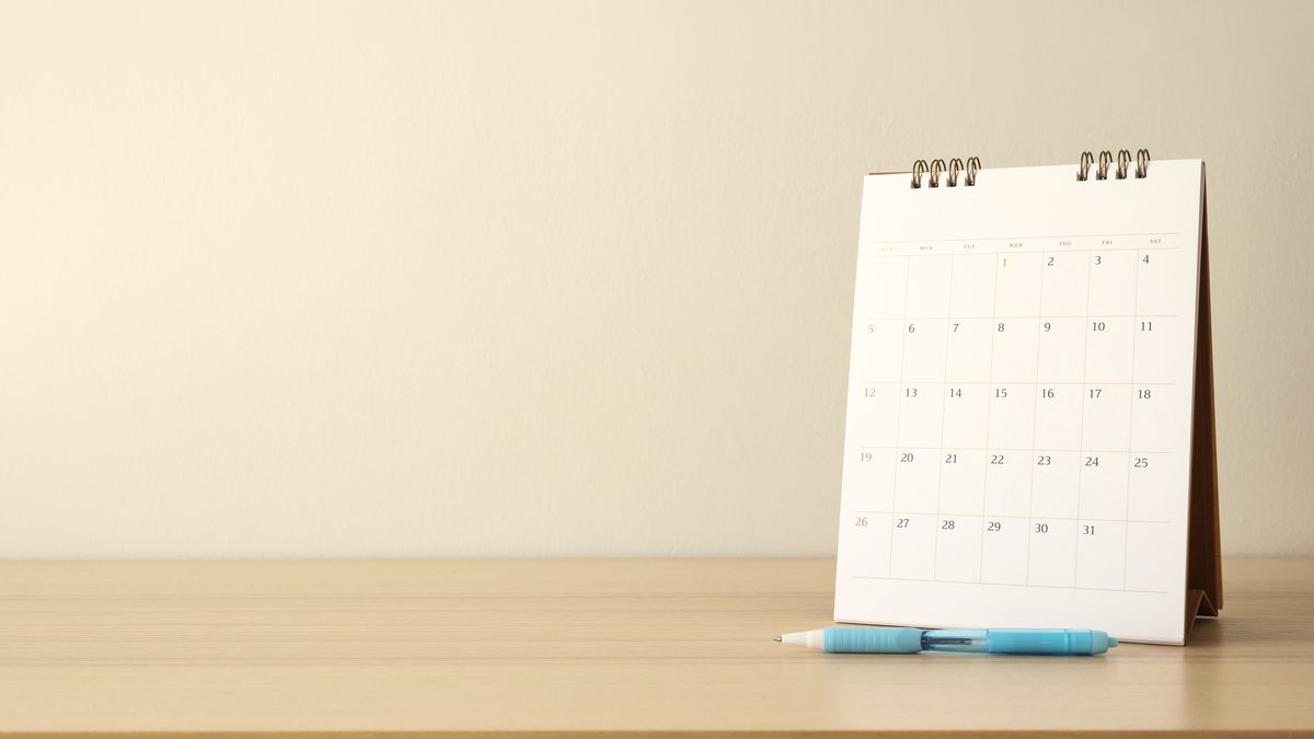 Calendrier de bureau posé sur une table en bois clair, à côté d'un stylo