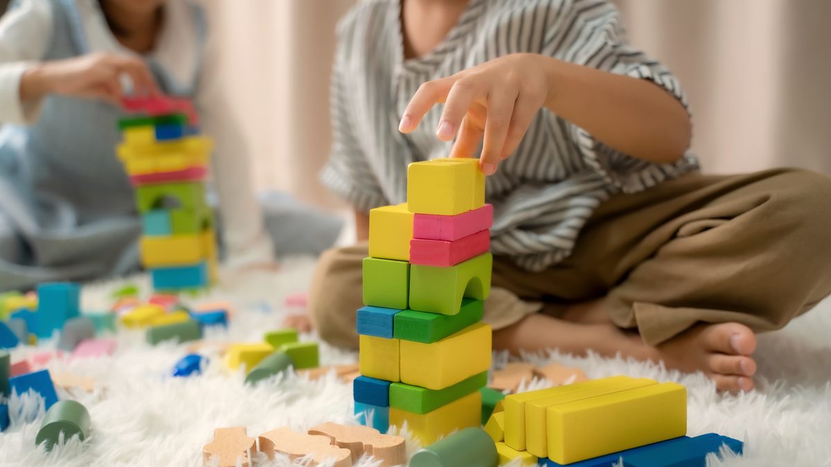 Mains d'un jeune enfant qui empile des cubes en bois colorés assis sur un tapis, activité sans écran