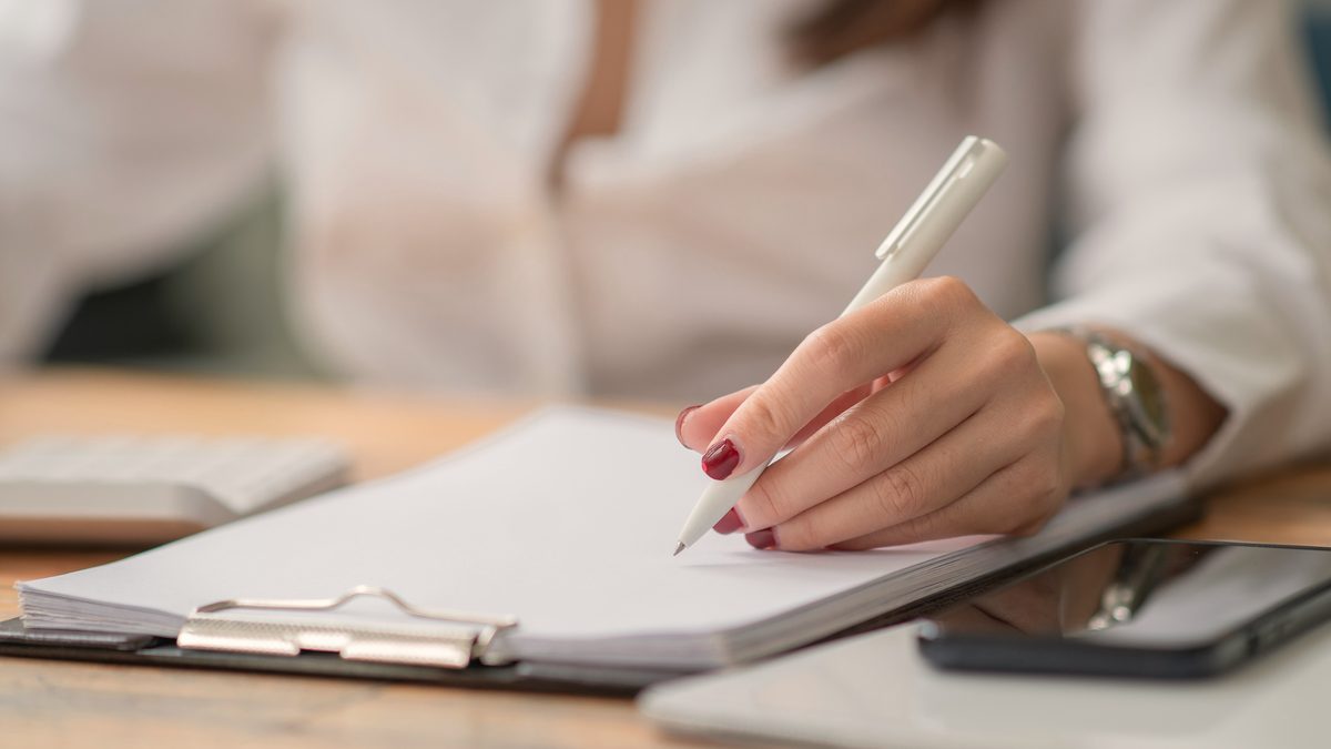 Main de professionnelle écrivant au stylo sur un document posé sur un porte-bloc