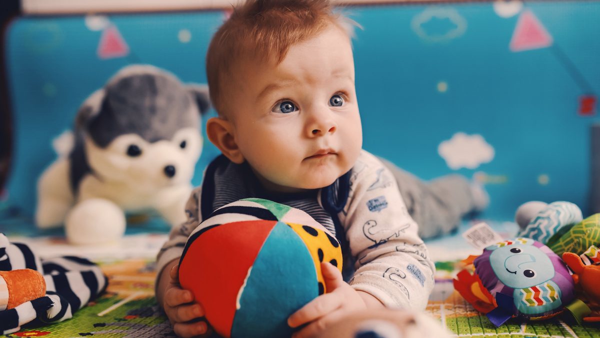 Un bébé allongé sur le ventre sur un tapis de jeu, concentré sur une balle en tissu qu'il tient entre ses mains