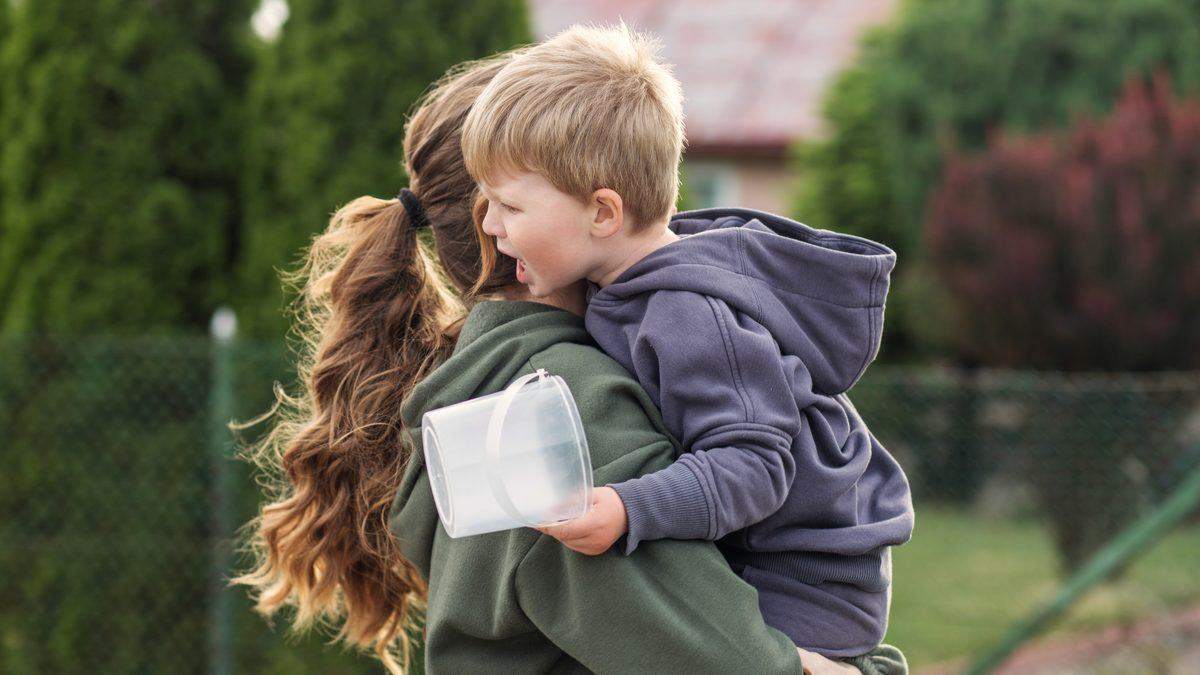 Parent portant dans ses bras un jeune enfant en pleine colère, à l'extérieur