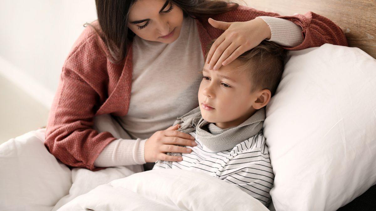 Mère posant la main sur le front de son jeune fils allongé sous une couverture à la maison