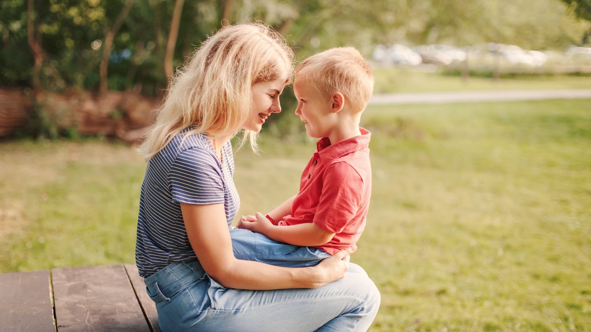 Une mère et son jeune fils face à face, front contre front, dans un moment d'échange calme en extérieur