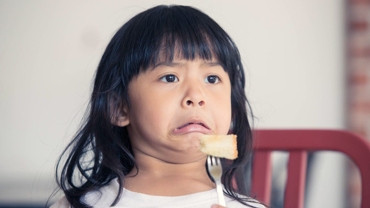 Jeune enfant attablé, fourchette à la main, faisant la moue devant une bouchée qu'il n'a pas envie de goûter