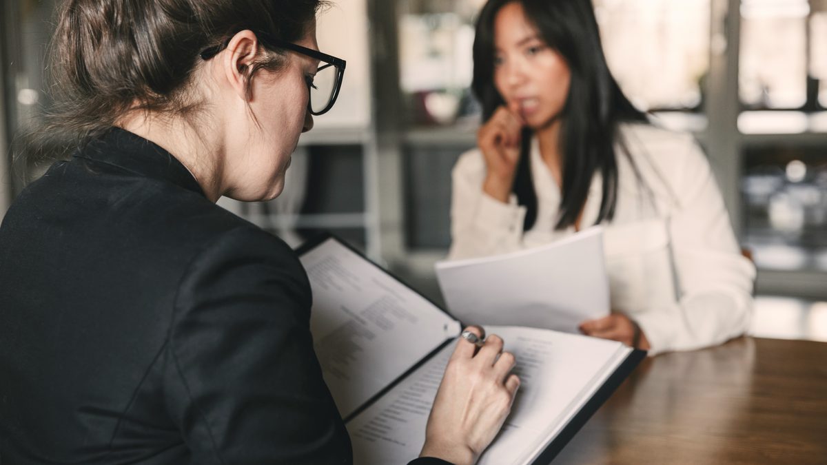 Deux femmes en entretien face à face dans un bureau clair, l'une prenant des notes sur un dossier