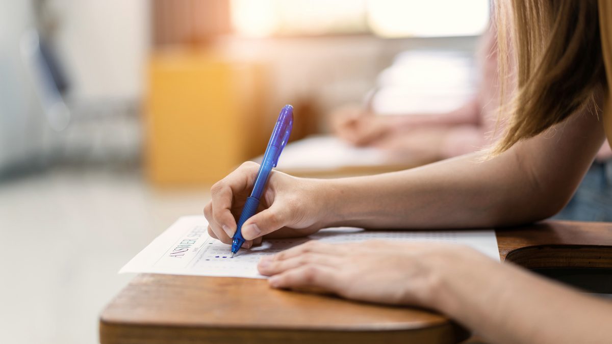 Gros plan sur la main d'une candidate qui écrit sa copie pendant une épreuve d'examen en salle